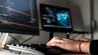 Person beim Programmieren an einem Arbeitsplatz mit zwei Bildschirmen.