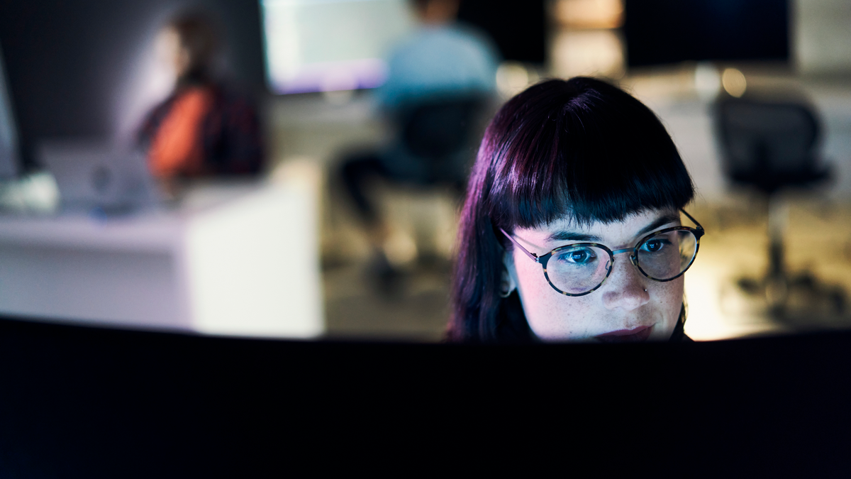 Person arbeitet konzentriert an einem Bildschirm in dunkler Büroumgebung