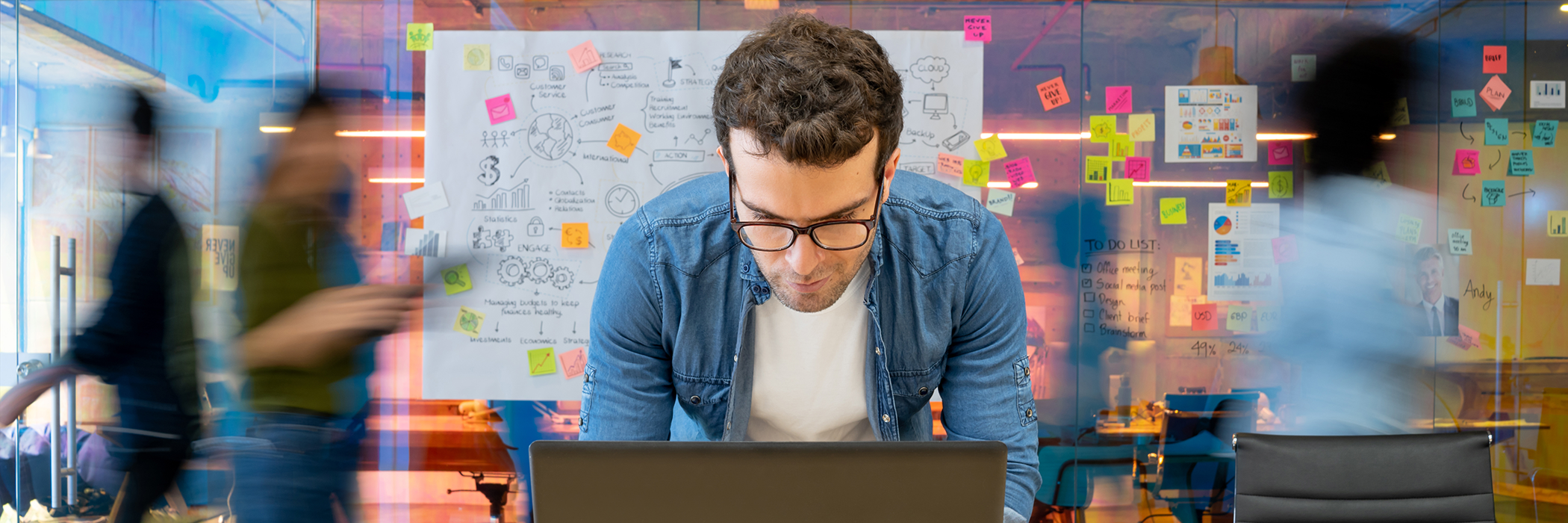 Person arbeitet konzentriert am Laptop in kreativem, farbig gestaltetem Büro mit Notizzetteln im Hintergrund.