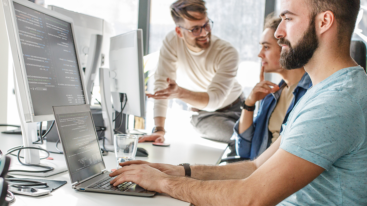 Drei Personen coden und besprechen sich in einem Büro-Setting.