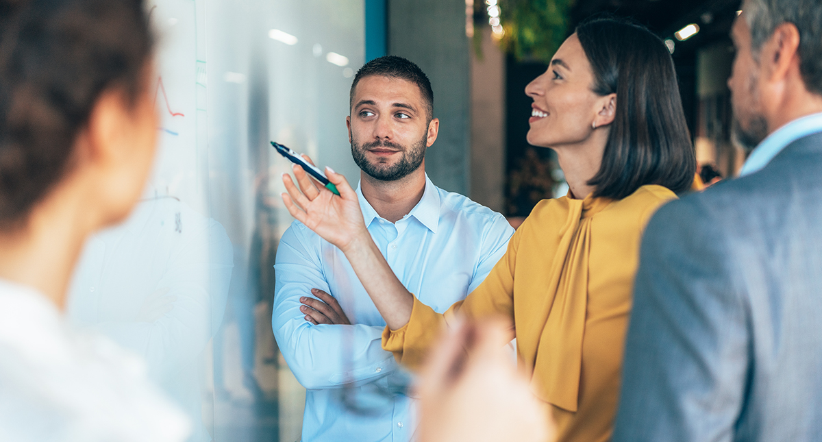 coworkers in a startup brainstorming strategies, writing a business plan on whiteboard to his team on a meeting
