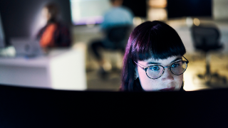 Person arbeitet konzentriert an einem Bildschirm in dunkler Büroumgebung