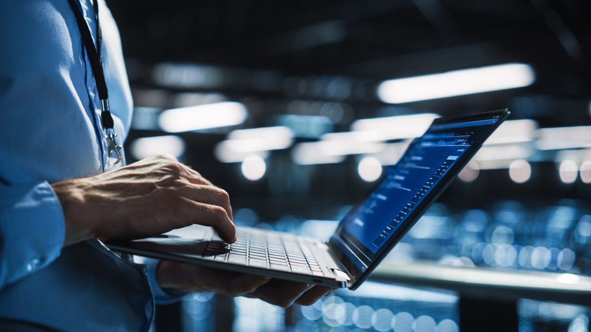 Person tippt auf Laptop mit geöffnetem Codefenster in moderner Umgebung